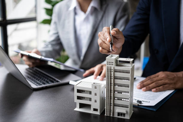 Two business professionals discuss urban development plans over architectural models in an office setting.