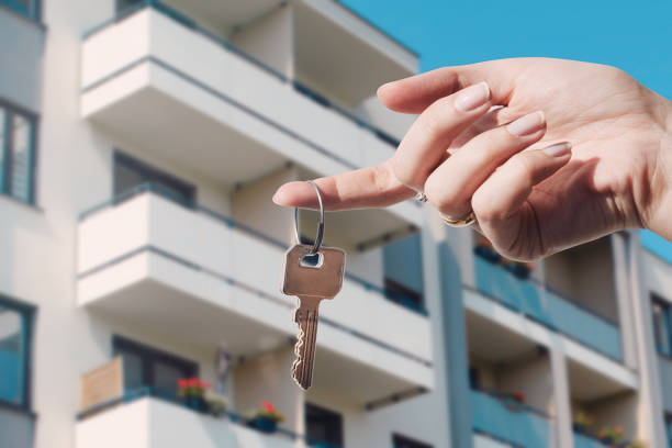 A hand holding a key with an apartment building in the background.