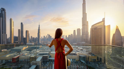 A woman in a red dress overlooks a city skyline with modern skyscrapers at sunset, emphasizing Binghatti Hills' urban locale.